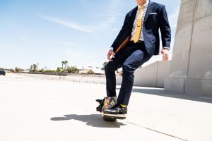 A man dressed in a suit is riding a one-wheel board outdoors. The background shows a park with trees and greenery, and there are no other people in the shot. Visual storytelling is a powerful tool for personal branding, and a creative director can help bring your brand story to life through compelling visuals.